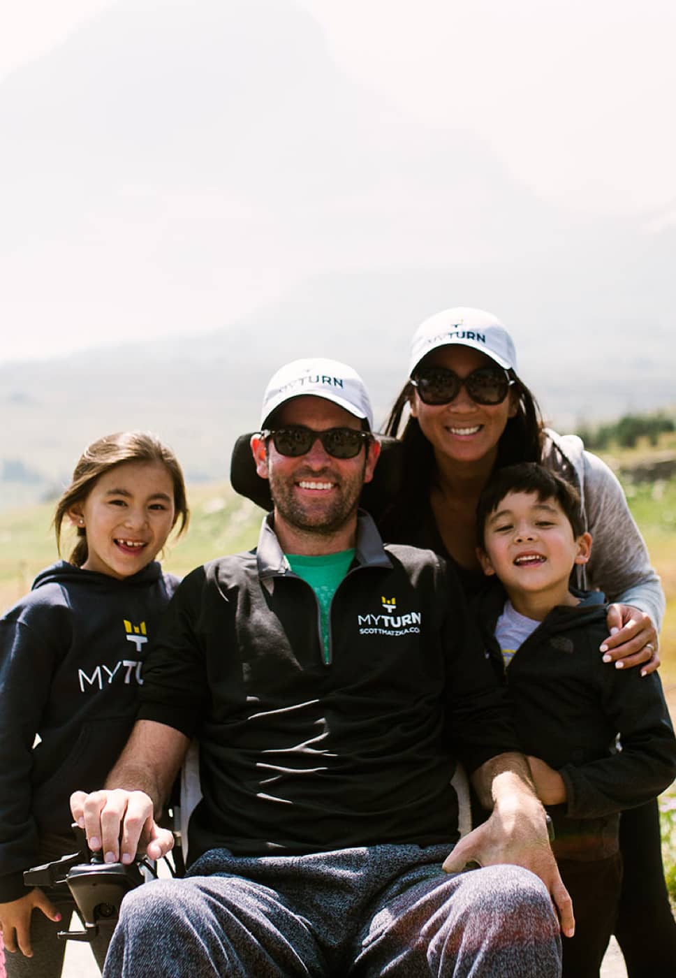 Scott Matzka in his wheelchair, beside his wife Katie and their two children. They're all smiling.