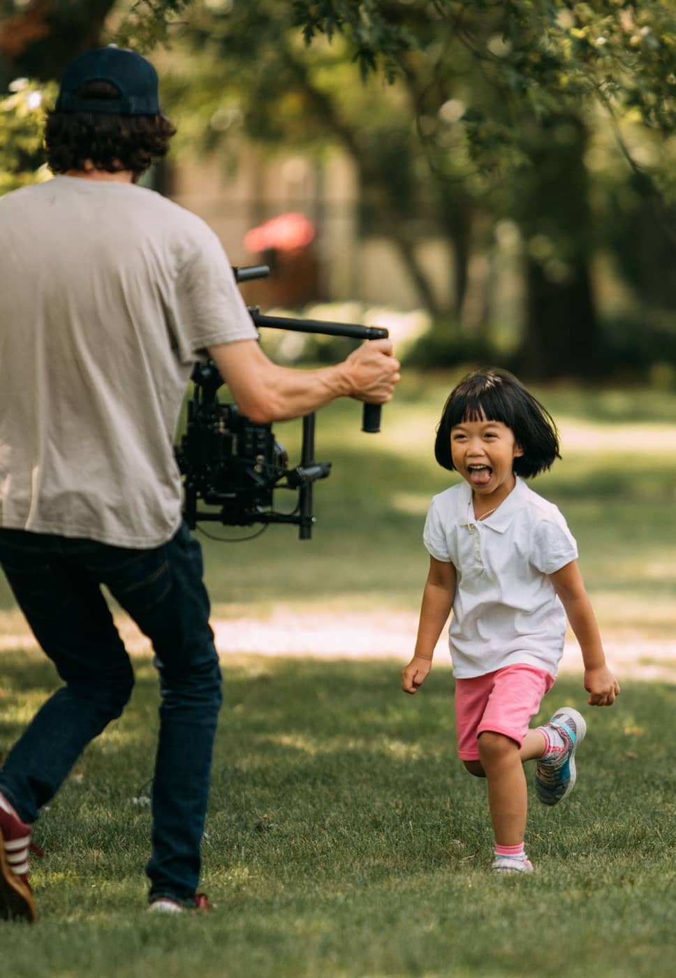 Our Media Producer Jared on set filming a smiling young girl running through the park